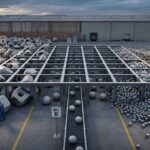 An industrial yard with workers sorting large geometric shapes—irregular objects, spheres, and cubes—into distinct groups, reflecting a One Template approach. Signs labeled BU A, B, and C hint at SAP Harmonisation Programmes across Multiple Businesses. A warehouse stands behind.